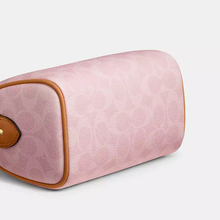 The Tiny Bag Coach Mini Rowan Crossbody Bag in signature powder pink with charms, featuring a compact design and adjustable strap.