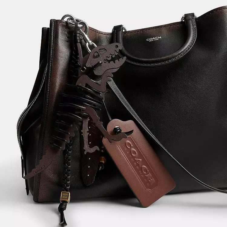 Coach Rogue shoulder bag in loved leather with charms, featuring a stylish design and spacious interior from The Tiny Bag.