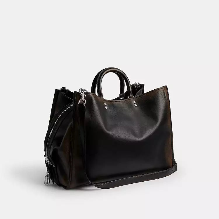 The Tiny Bag Coach Rogue Shoulder Bag in loved leather with charms, featuring a sleek design and decorative accessories.