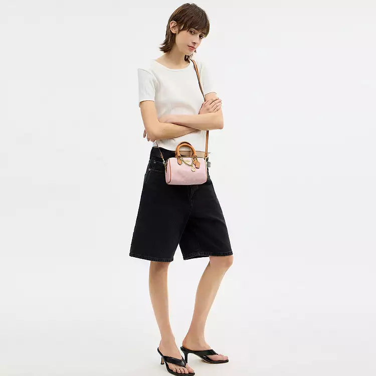 Coach Mini Rowan Crossbody Bag in signature powder pink leather with charms, featuring a compact design and adjustable strap.