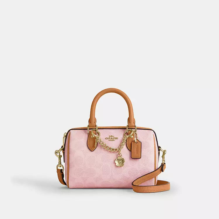 The Tiny Bag Coach Mini Rowan Crossbody Bag in Powder Pink signature leather with charms, small and stylish for everyday use.