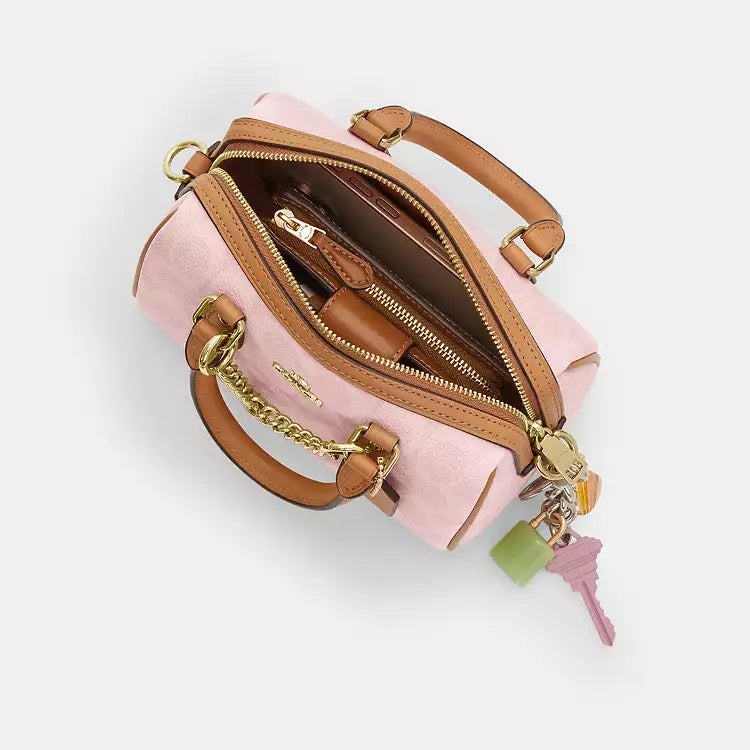 The Tiny Bag Coach Mini Rowan Crossbody Bag in signature powder pink with charms, featuring a compact design and adjustable strap.