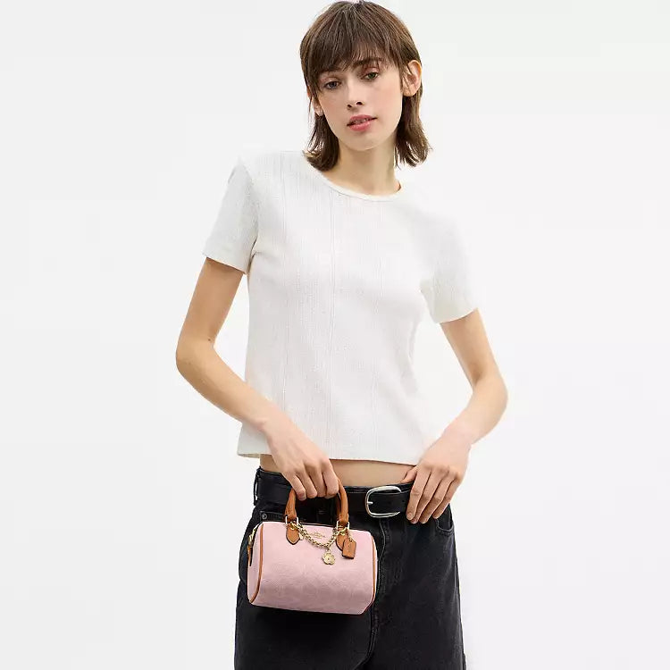 The Tiny Bag Coach Mini Rowan crossbody bag in signature powder pink with charms, featuring a compact leather design and adjustable strap.