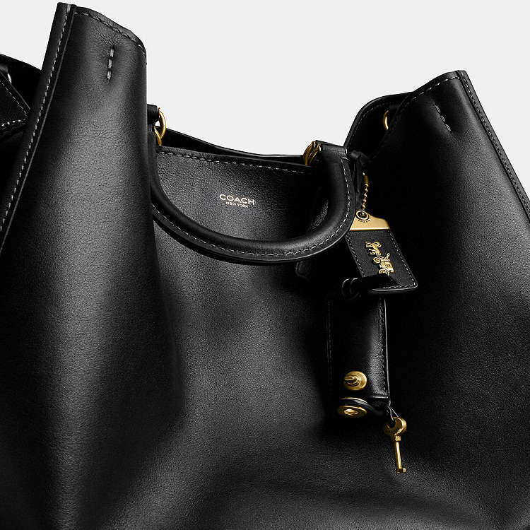 Black leather COACH Rogue Bag 40 crossbody with CCX21 logo, featuring sleek design and adjustable strap from The Tiny Bag.