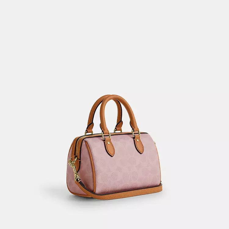 The Tiny Bag Coach Mini Rowan Crossbody Bag in signature leather with charms, in powder pink, featuring a compact design and adjustable strap.